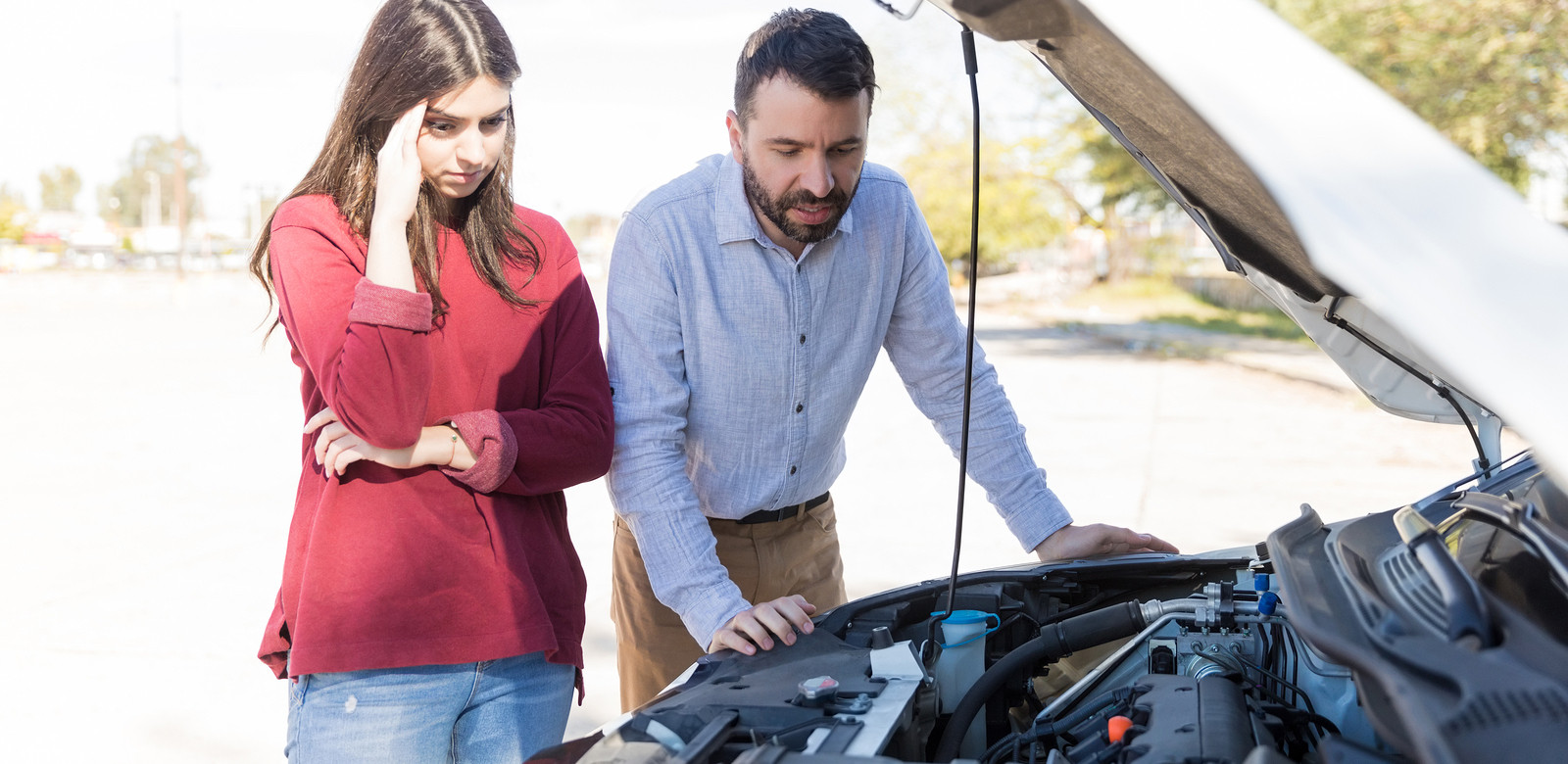 Worried-looking lady and bearded man staring at car engine